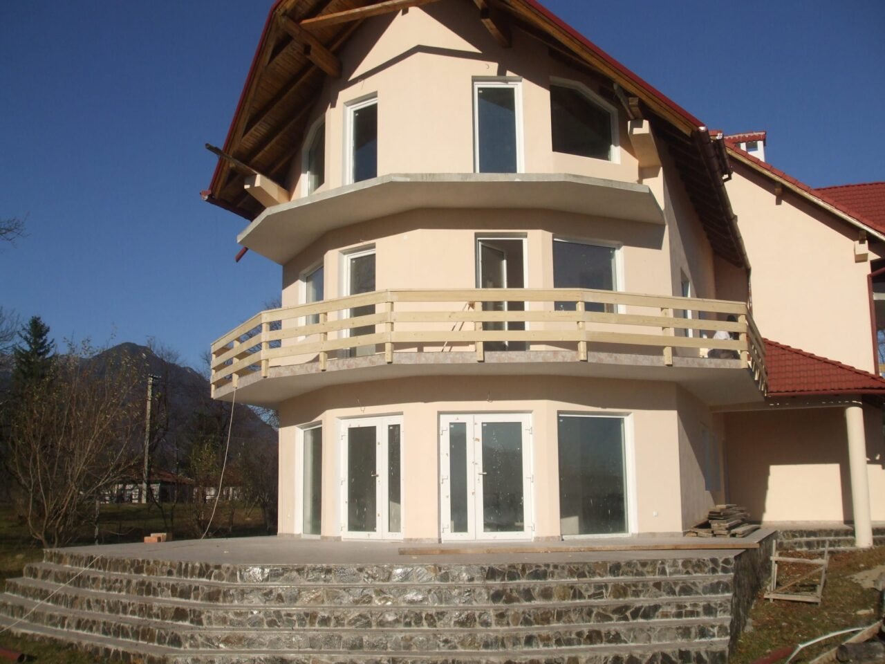 Casă cu balcon rotunjit și balustradă din lemn vopsit alb, cu munții în spate