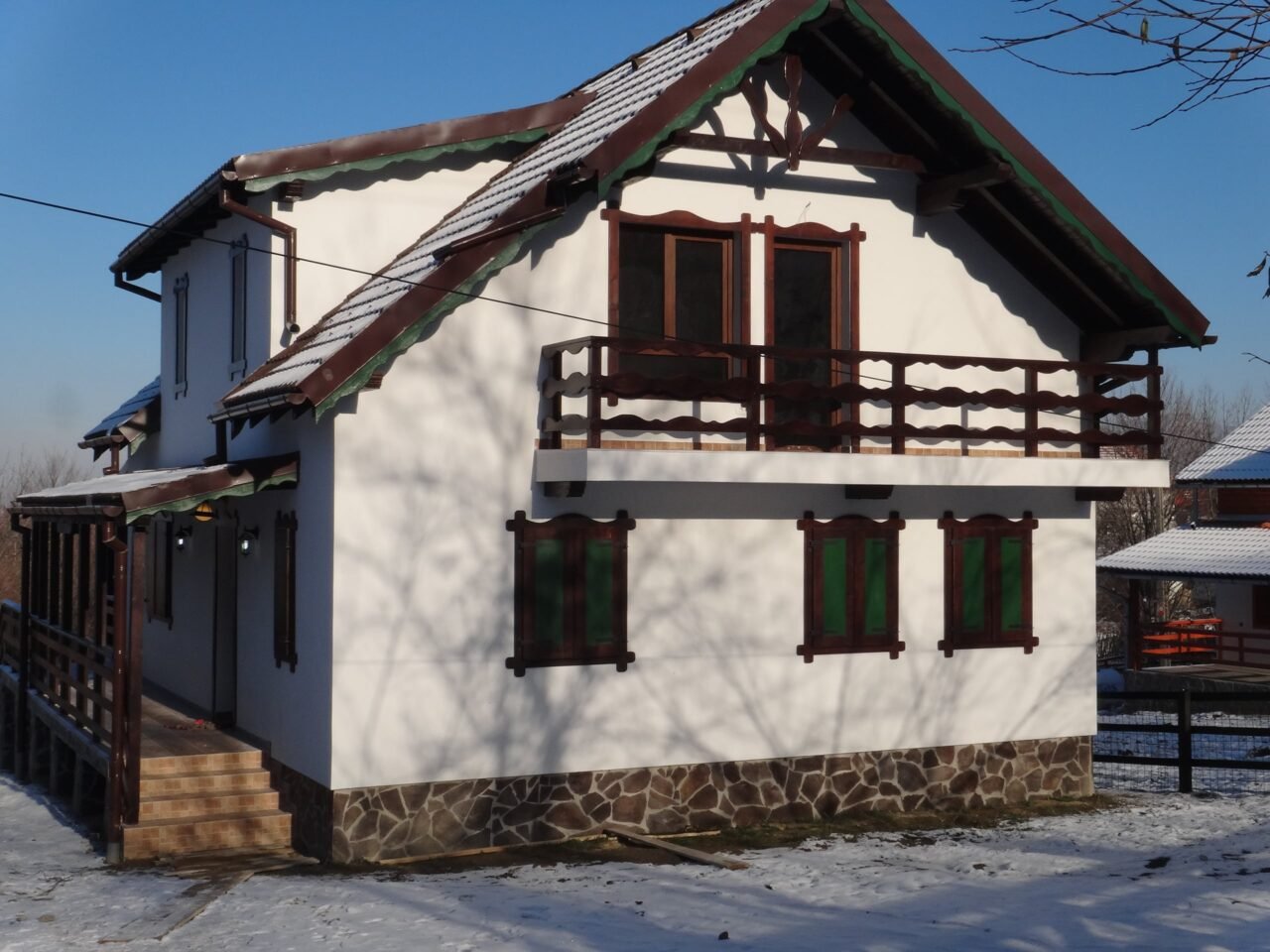 Casă albă cu balcon din lemn închis la culoare și obloane din lemn, iarna