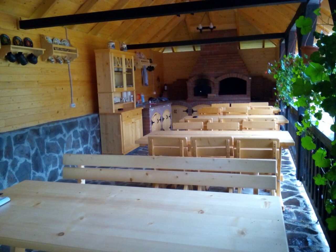 Foișor cu mese și bănci din brad natur, cu grătar de zidărie în fundal